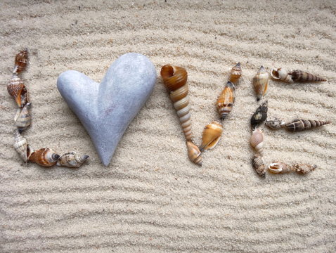 inscription Love with shells on gray sand - selective focus, useful as a background