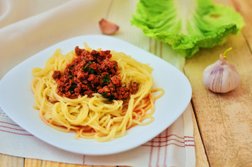 Spaghetti with meat in tomato sauce on a white plate. A plate of spaghetti on a napkin on a wooden background