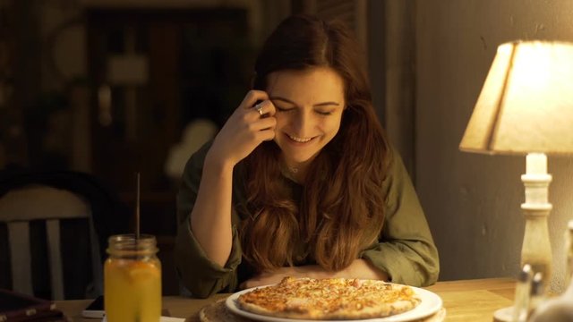 Girl smelling pizza and smiling to the camera in the cafe
