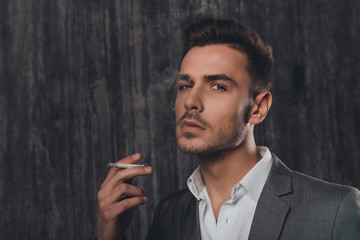Handome businessman in suit  smoking a cigarette on gray backgro