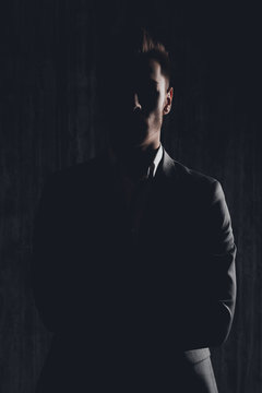 Dark photo of serious man in suit posing with crossed hands