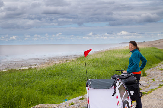 Junge Frau fährt Fahrrad mit Anhänger auf dem Nordseeküstenradweg