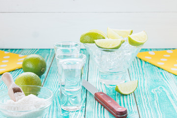 tequila in glasses and  lime fruits on turquoise colored wooden table