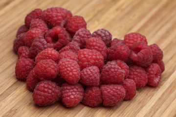 Big heart from many raspberries on the wooden kitchen board.