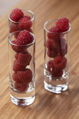 Many raspberries in three long shot glasses on the wooden board