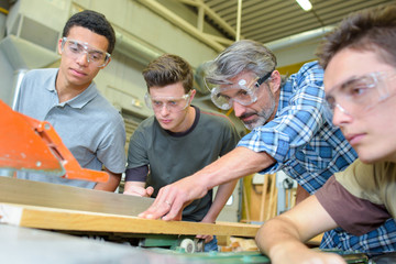 Carpenter showing apprentices how to use machinery