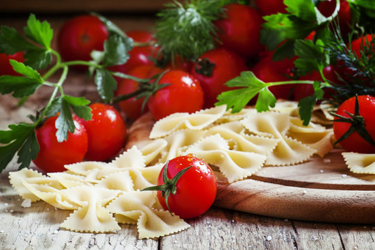 Dry Italian pasta farfalle, cherry tomatoes, vintage wooden back