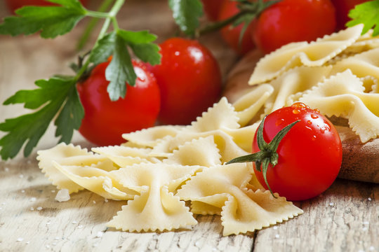 Dry Italian pasta farfalle, cherry tomatoes, vintage wooden back