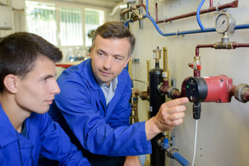 Plumber showing pipework to apprentice