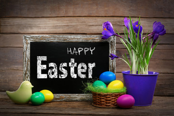 Easter greeting card. Colorful eggs with flowers and blackboard on wooden background