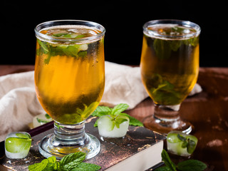 Cold tea with ice and mint leaves on dark background
