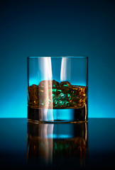 A glass of whisky on a reflective bar top surface with edge highlights.