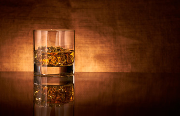 A glass of whisky on a reflective bar top surface with edge highlights.