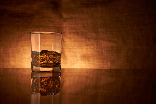 A Glass Of Whisky On A Reflective Bar Top Surface With Edge Highlights.