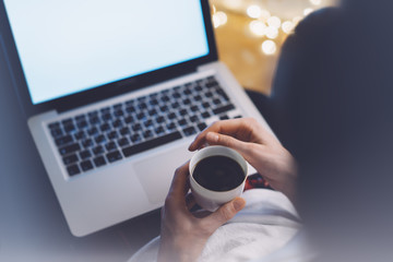 Girl in a relax atmosphere with an open laptop with a empty blank screen monitor and a cup of coffee or tea on the background bokeh light, freelancer working and using digital computer 