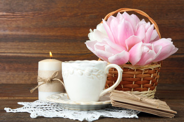 fragrant lilac flowers in wicker basket beside the coffee Cup and book with candle on wooden background