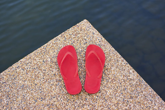pair of red comfortable slipper placed lake side of stony floor