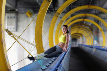 Sexy fitness girl sitting on the handrail of a bridge