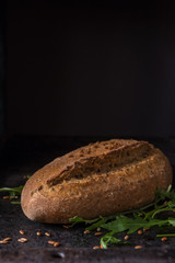 Black food background with homemade bread loaf and  fresh aromatic ruccola , copy space. Top view