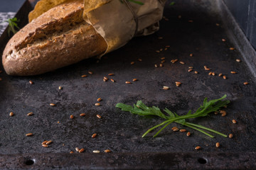 Black food background with homemade bread loaf and  fresh aromatic ruccola , copy space. Top view