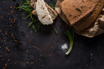 Black food background with homemade bread loaf and  fresh aromatic ruccola , copy space. Top view