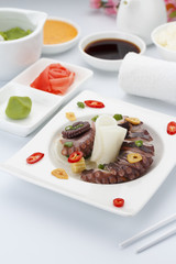 Salad with octopus on a white plate with ginger wasabi and sauces.