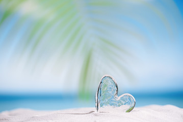 clear glass heart on white sand beach