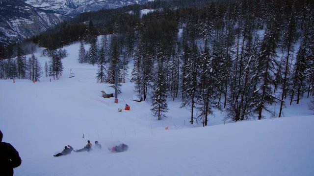 Cheerful group of teenagers takes a sledding ride down the ski slope and have fun times after skiing day. Recorded at dusk.
