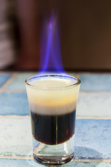Shooter - B52 cocktail - layered and with the flame on the bar - table with blue ceramic tiles.