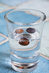 Coffee liqueur in a shot glass with three coffee beans inside on the bar - table with blue ceramic tiles.