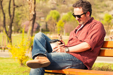 Naklejka na ściany i meble Man with smartphone and coffee sitting on a bench