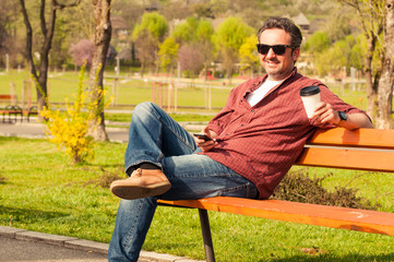Handsome young man sitting in park on wooden bench