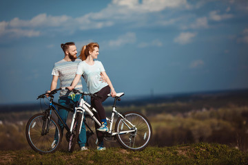 Fototapeta na wymiar Beautiful young couple in love walking with bicycles hugging and looking towards the beautiful nature and the blue sky. The concept of active rest