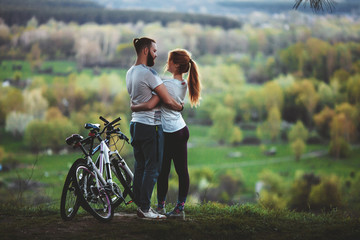 Beautiful young loving couple hugging at sunset, there are two bikes. The concept of happiness, peace and love