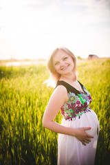 Naklejka na ściany i meble A young pregnant woman in a wheat field Concept photo of pregnancy, pregnant woman