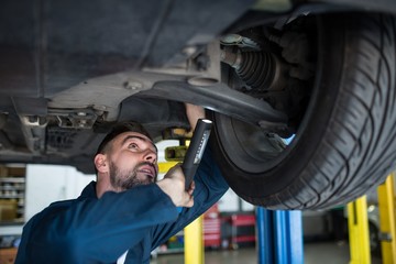 Mechanic examining car tyre using flashlight at the repair garage