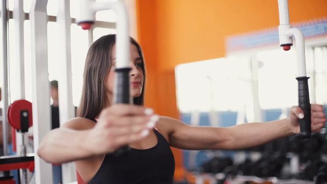 young woman flexing muscles on cable gym machine.