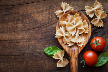 Italian cuisine concept - Wholemeal farfalle pasta in wooden spoon with fresh basil and tomatoes od...