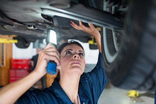 Female mechanic examining car using flashlight