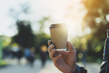 Close-up of male hand holding coffee to take away at early morning in park, flare light