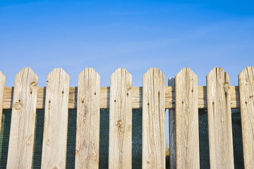 Fototapeta premium Detail of a wooden fence built with spiky wooden boards against a blu sky