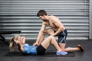 Naklejka premium Male trainer assisting woman with sit ups