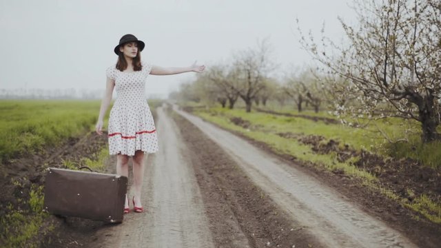 young woman dressed in retro style hitch-hiking on the country road slow motion
