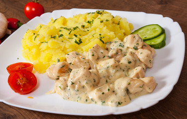 chicken breast in a creamy sauce with mashed potatoes in a plate on wooden table