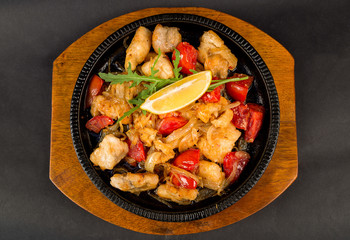 Frying-pan with slices of fish, tomatoes, onions and lemon