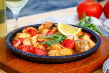 Frying-pan with slices of fish, tomatoes, onions and lemon