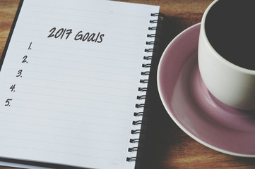 Words and number 2017 new year's goals list on notepad with cup of coffee, retro style background.