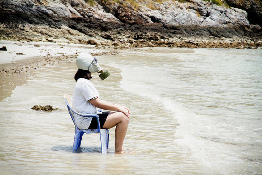 Girl with gas masks sitting on a chair at the sea.