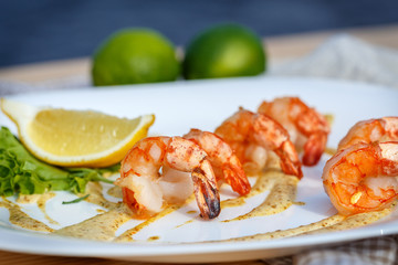 Grilled prawns with sauce and lemon on white plate.