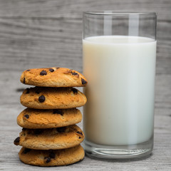 Glass of milk and chocolate cookies on gray wooden surface